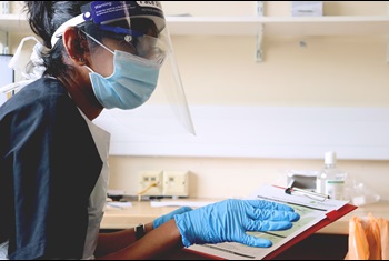 A doctor in full PPE in a doctor's office holding a clipboard